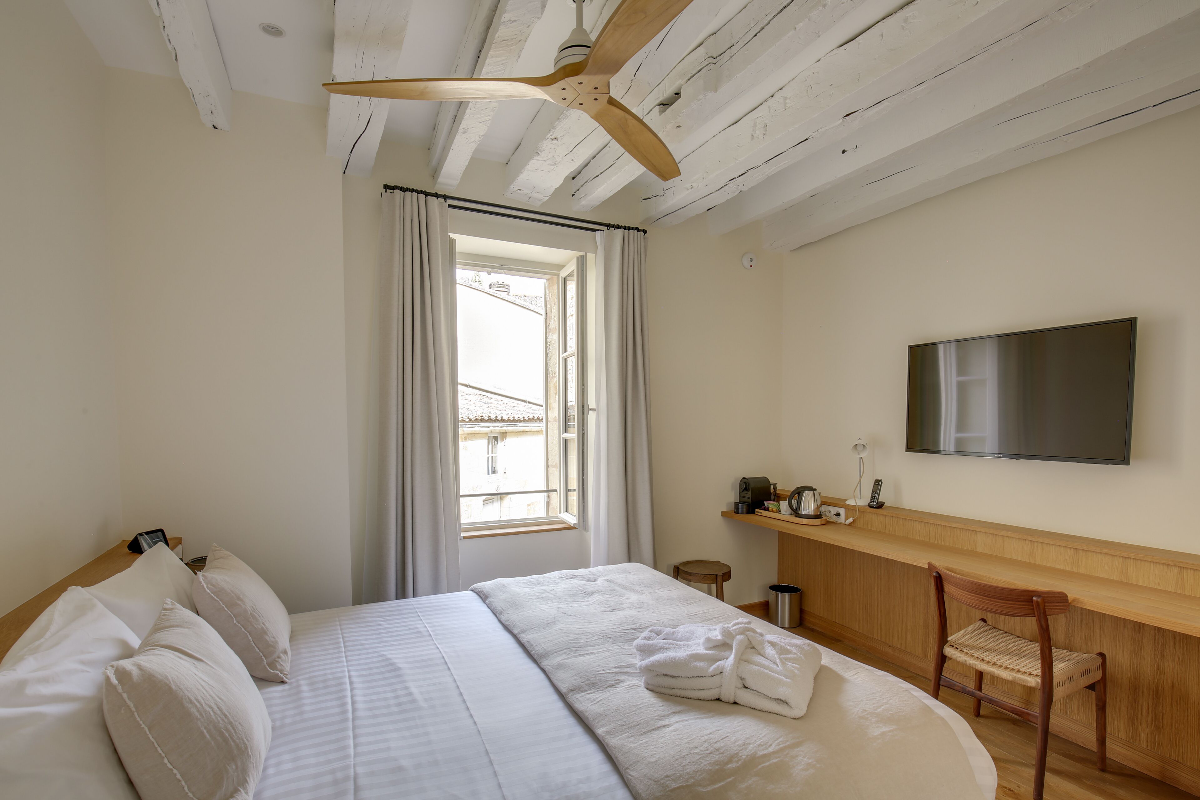 A hotel room with a bed, a wooden chair, a TV, and a window with curtains.