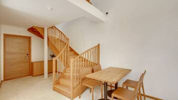 A spacious room with a wooden staircase, a dining table with chairs, and a door.