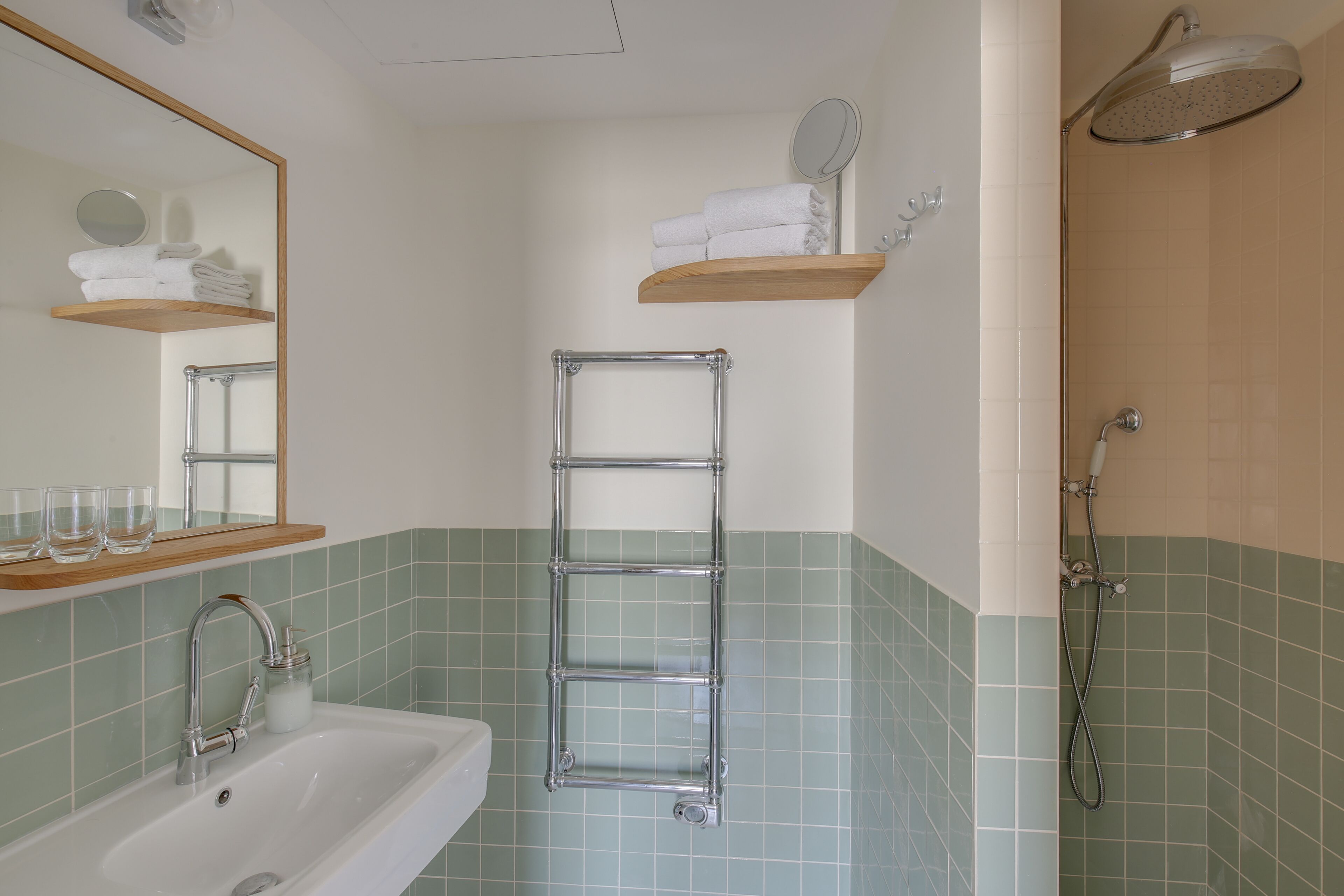 Un baño con lavamanos, espejo, toallero y ducha.