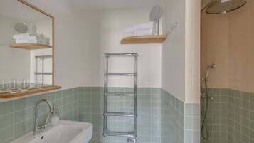 Un baño con lavamanos, espejo, toallero y ducha.