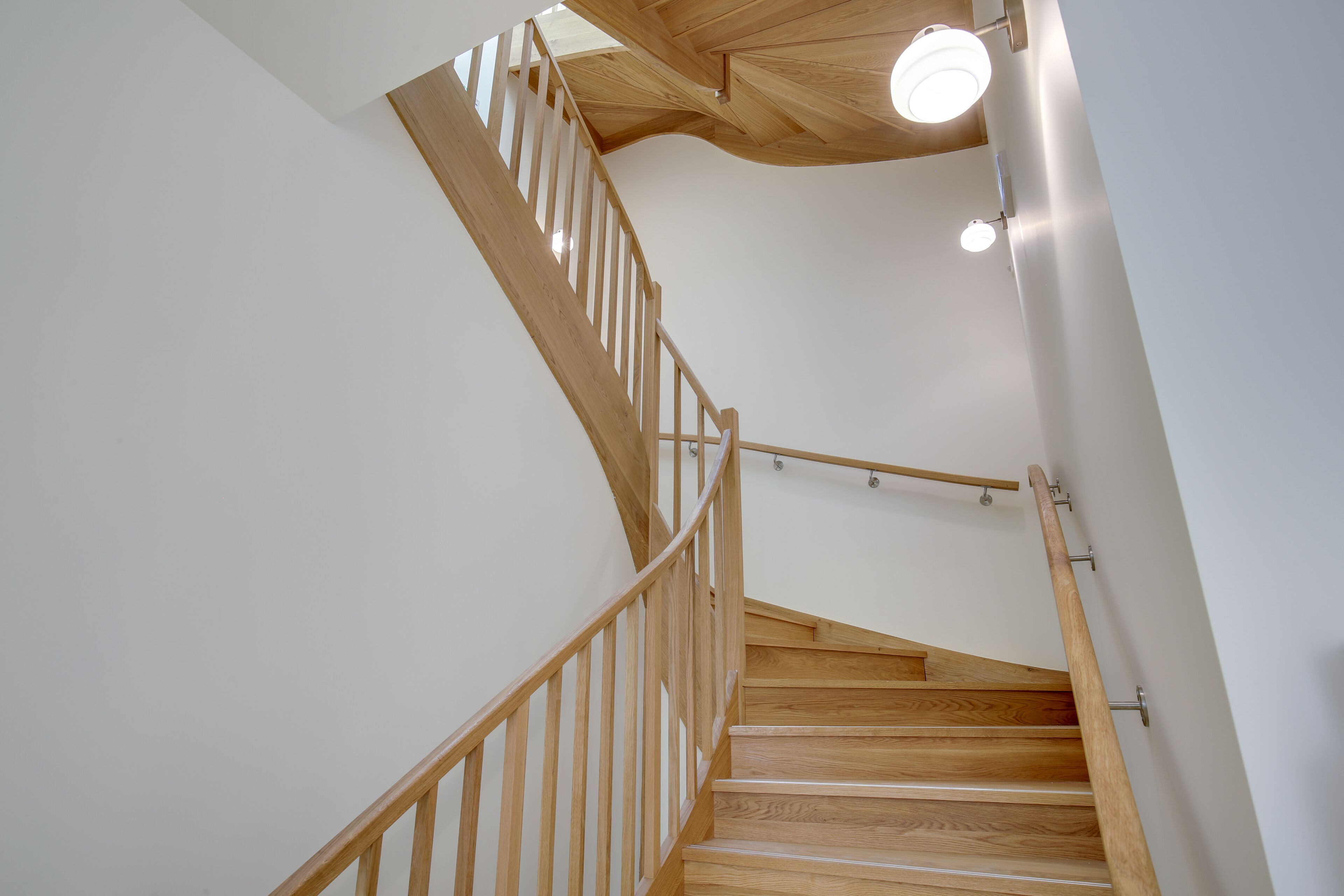 A wooden staircase with a handrail, white walls, and a ceiling light fixture.