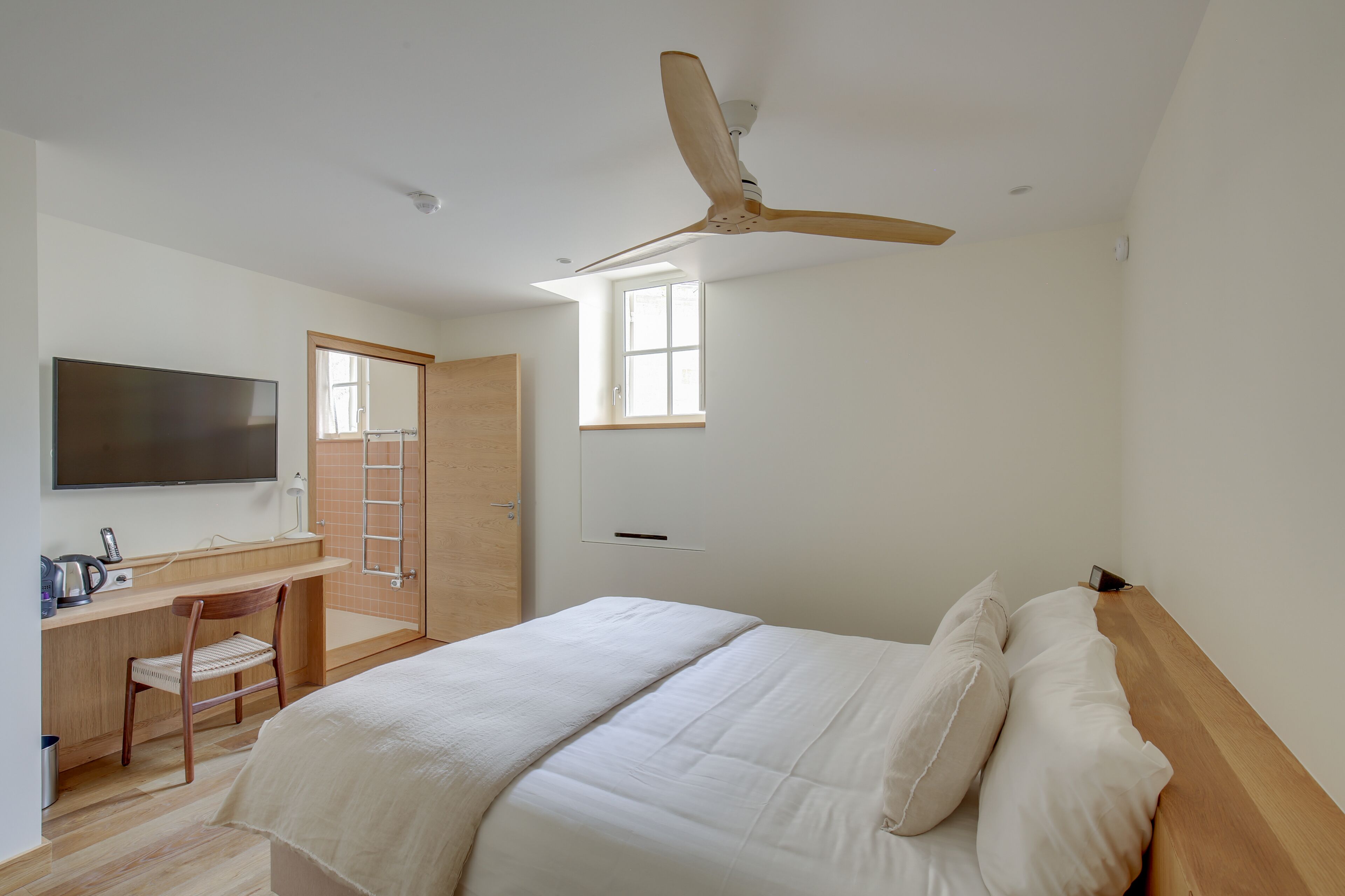A bedroom with a bed, a desk, a chair, a TV, and a ceiling fan.