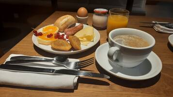 A breakfast setting with a plate of eggs, toast, sausage, and fruit, a glass of orange juice, and a cup of coffee on a wooden table.