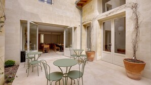 An outdoor patio with a table and chairs, a potted plant, and a view of the interior through glass doors. - Badon Boutique Hôtel (Saint-Émilion)
