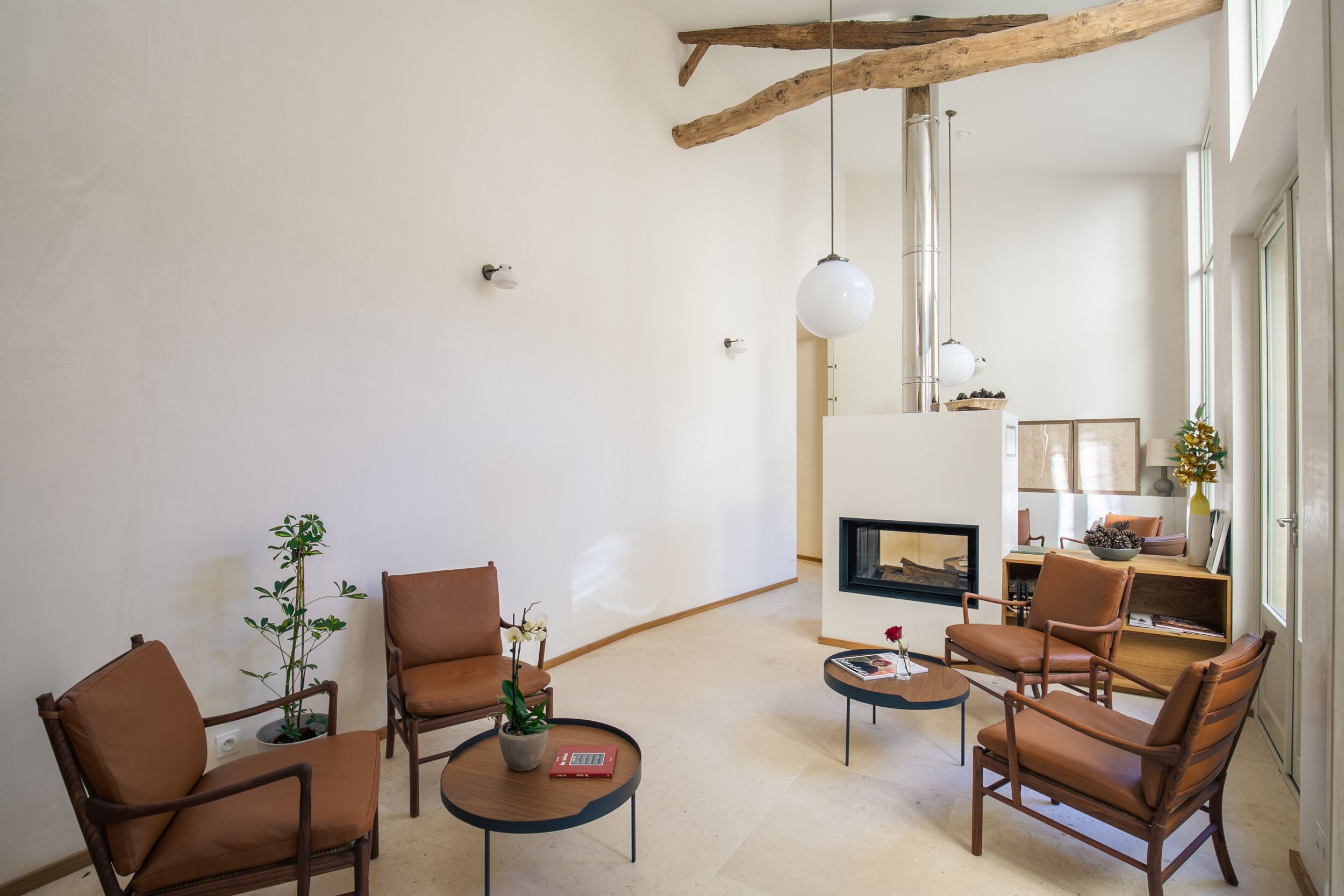 A modern living room with a fireplace, leather chairs, a coffee table, and a potted plant.