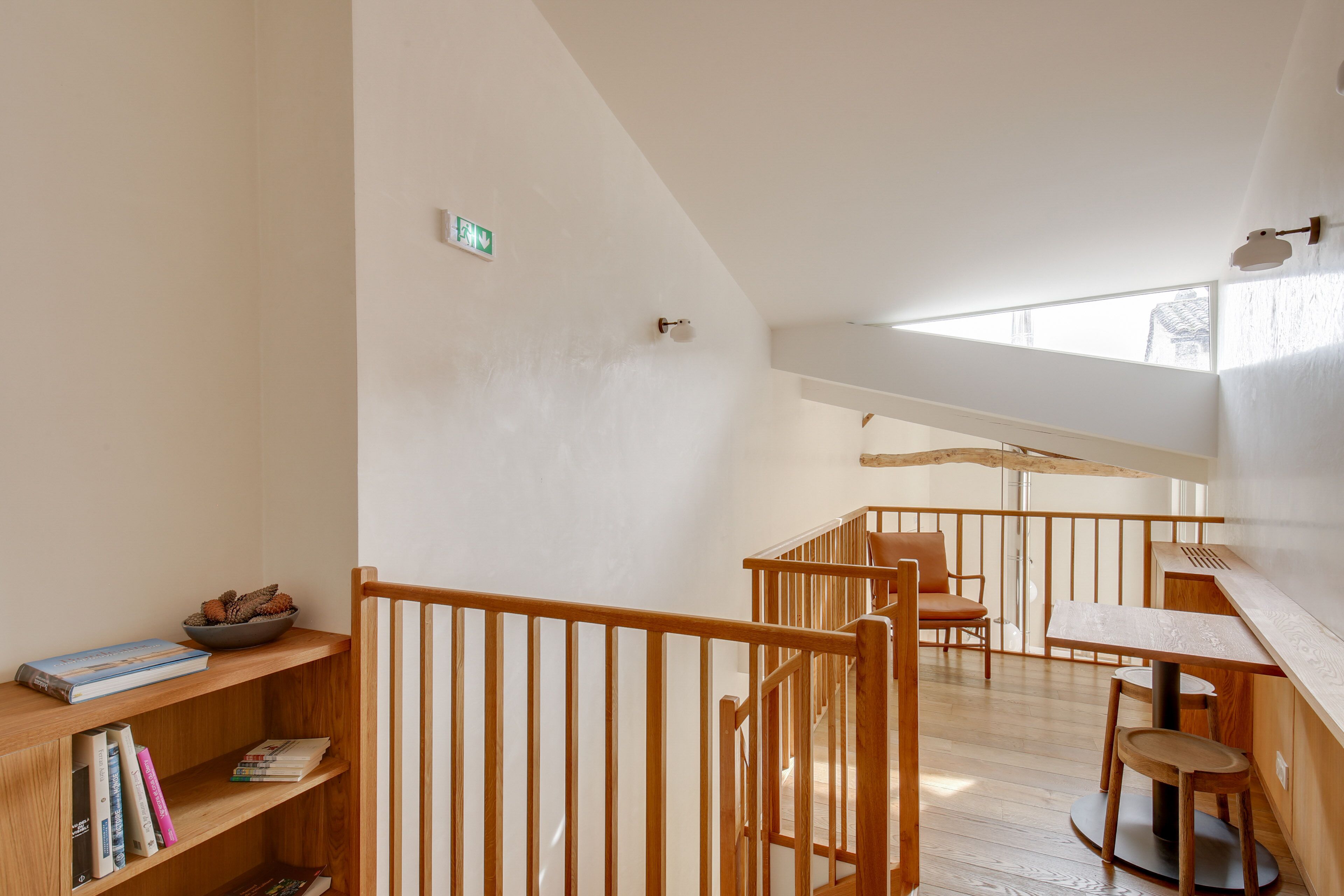 A spacious loft with a wooden staircase, a dining area, and a bookshelf with books and pinecones.
