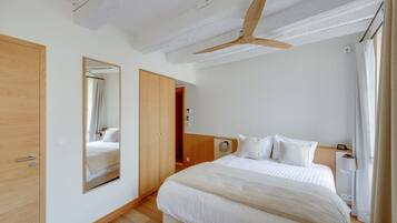 Un dormitori amb llit, ventilador de sostre, mirall i armari de fusta.