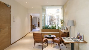 A modern hotel lobby with a wooden bench, two chairs, a small table with a plant, and a lamp on a desk. - Badon Boutique Hôtel (Saint-Émilion)