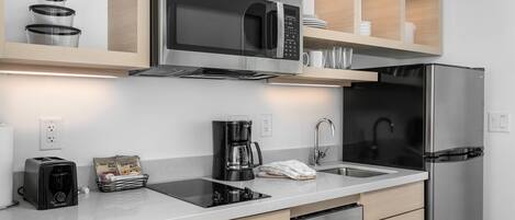 Una cocina moderna con un refrigerador de acero inoxidable, un microondas empotrado, una cafetera y un lavavajillas.
