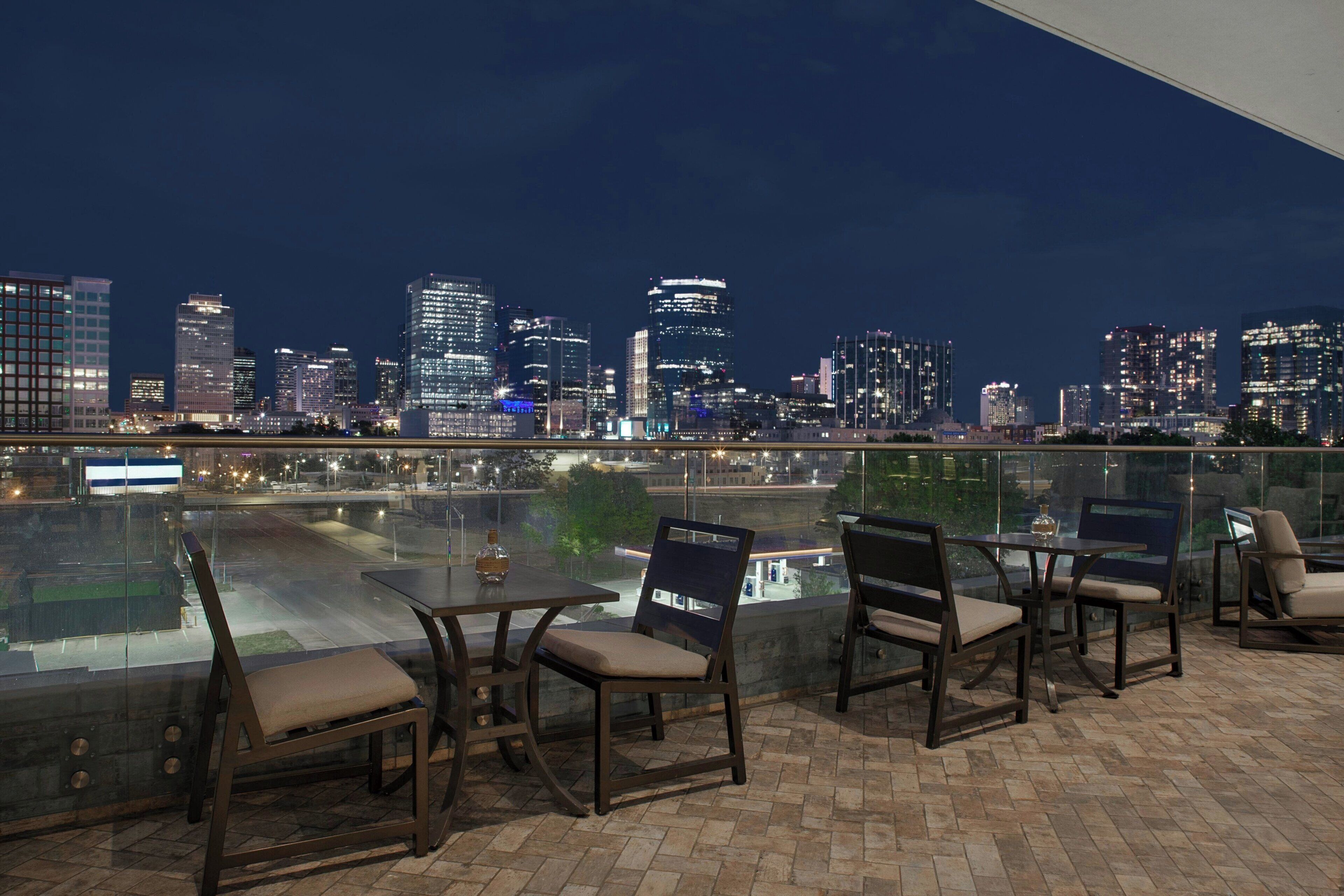A rooftop terrace with a city skyline view, furnished with chairs and a table.
