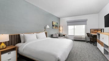 Habitación de hotel con una cama grande, un escritorio, una silla, un televisor y una ventana con vistas.