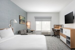 Habitación de hotel con una cama grande, un escritorio, una silla, televisión y ventana con vistas.