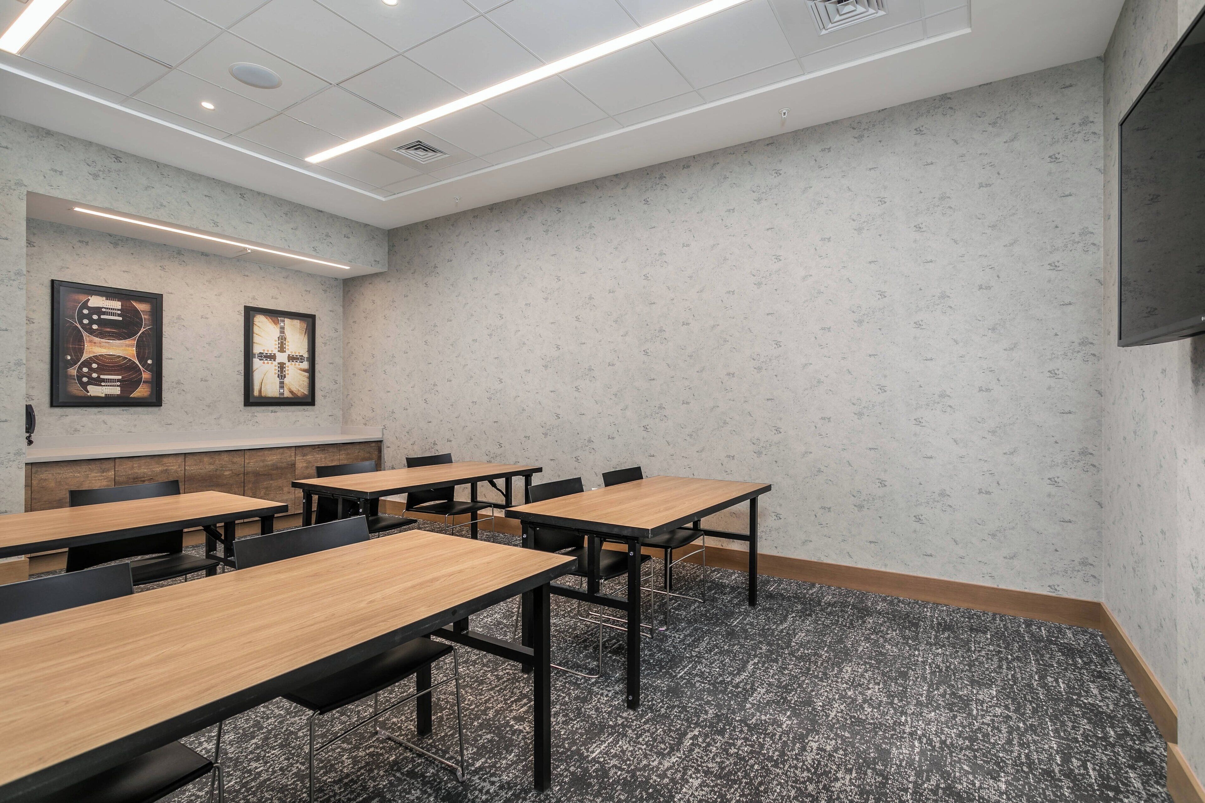 A conference room with multiple tables and chairs, a projector screen, and framed artwork on the wall.