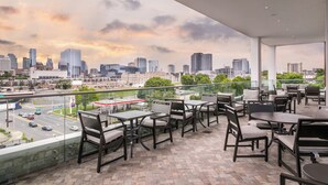 A balcony with outdoor seating, a city skyline view, and a gas station in the background.