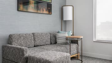 A modern living room with a grey sectional sofa, a small round table, a floor lamp, and artwork on the wall.