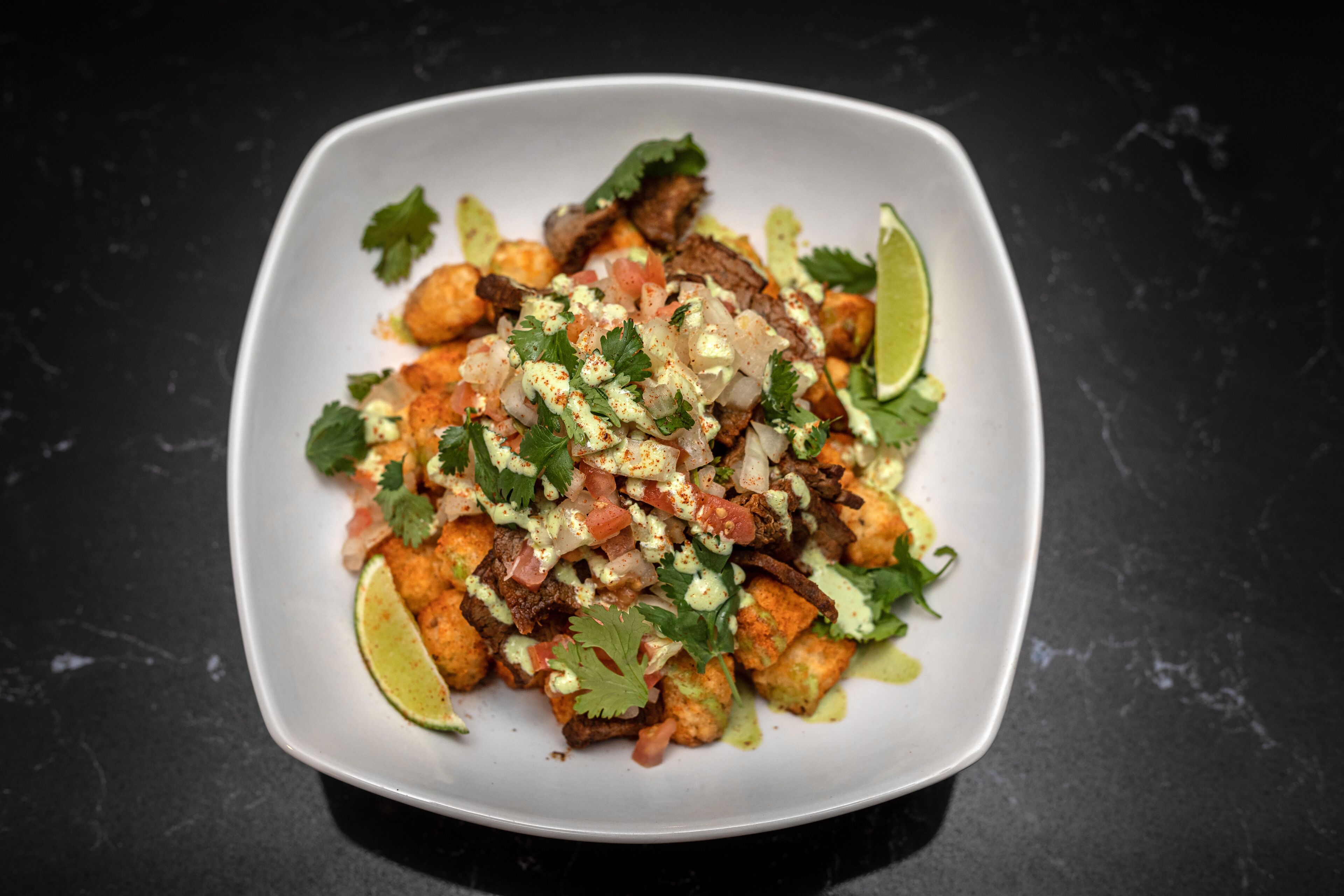 Un plato blanco cuadrado con un guiso de comida, adornado con cilantro y gajos de lima.