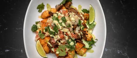 Un plato blanco cuadrado con un guiso de comida, adornado con cilantro y gajos de lima.