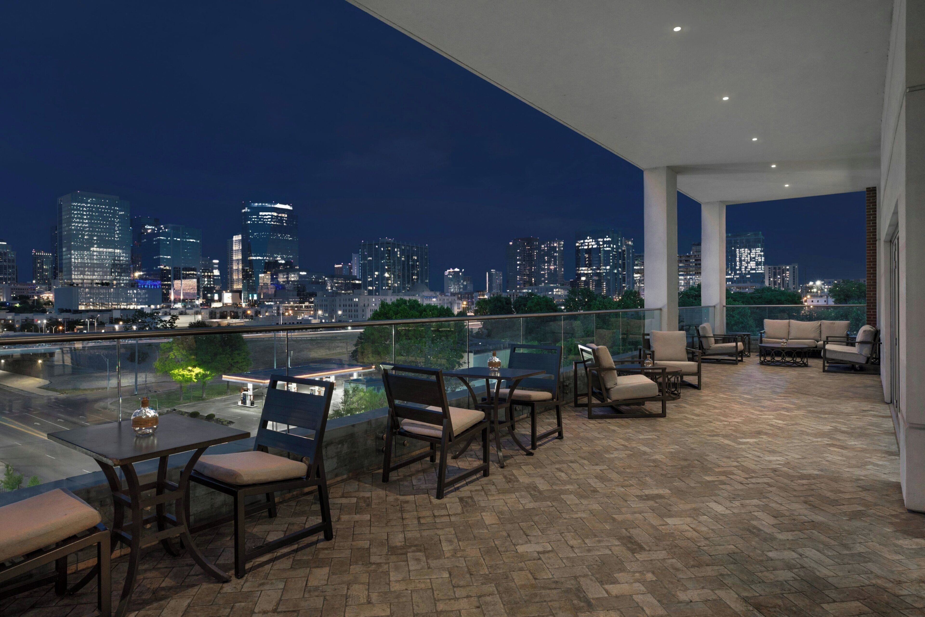 A rooftop terrace with a city skyline view, furnished with outdoor seating and a glass railing.