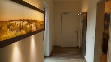 A hallway with a wooden floor, a framed picture of a landscape, and a door at the end.