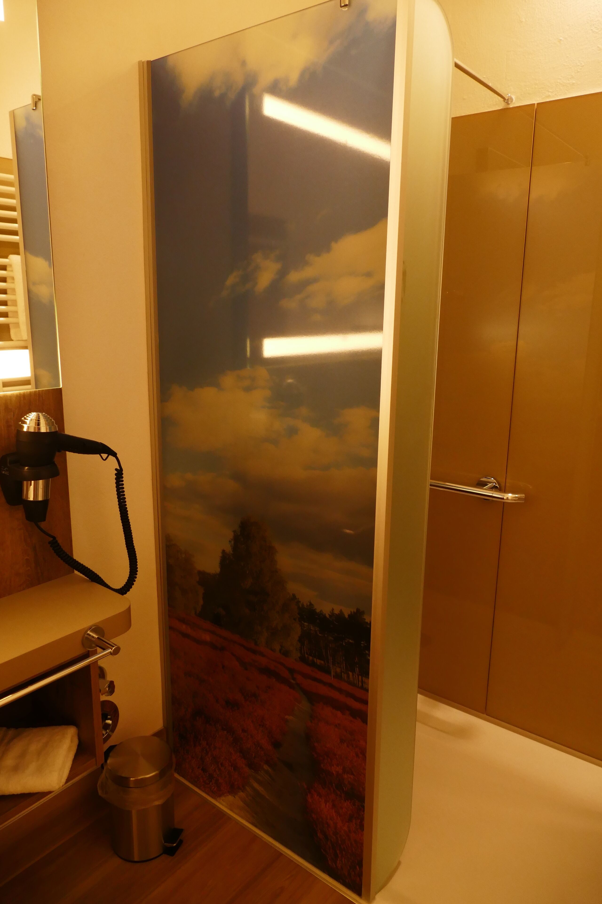 A bathroom with a shower curtain featuring a landscape design, a towel rack, a hairdryer, and a toilet.