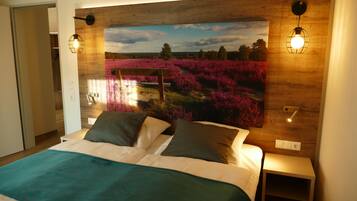 A bedroom with a large bed, two bedside lamps, and a wall-mounted painting of a field.