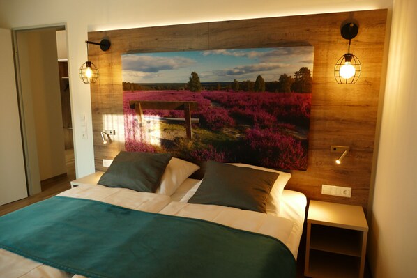 A bedroom with a large bed, two bedside lamps, and a wall-mounted painting of a field. - Meyn's Apartments & Hotel (Soltau)