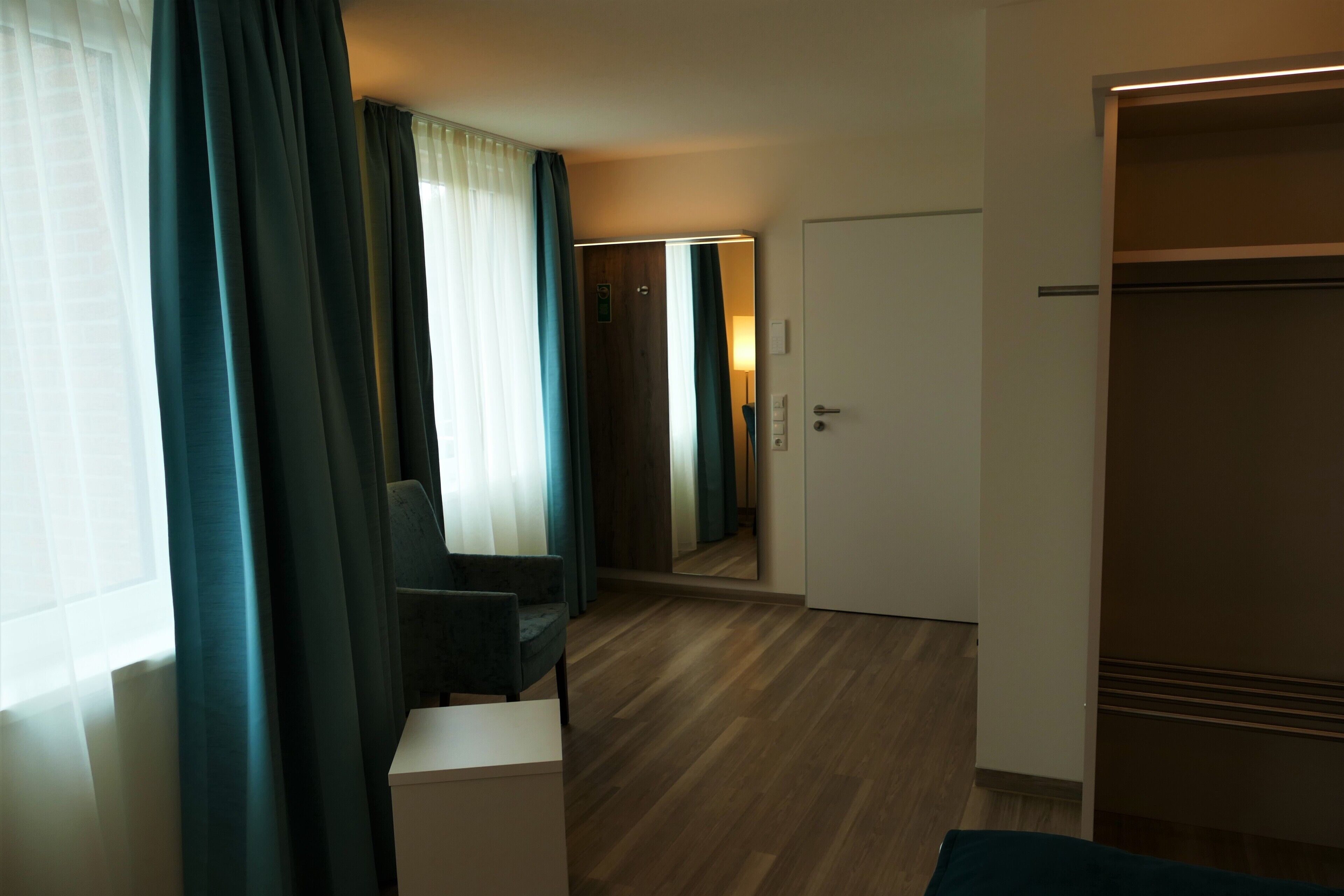 Habitación de hotel con piso de madera, una silla, un escritorio y un armario.