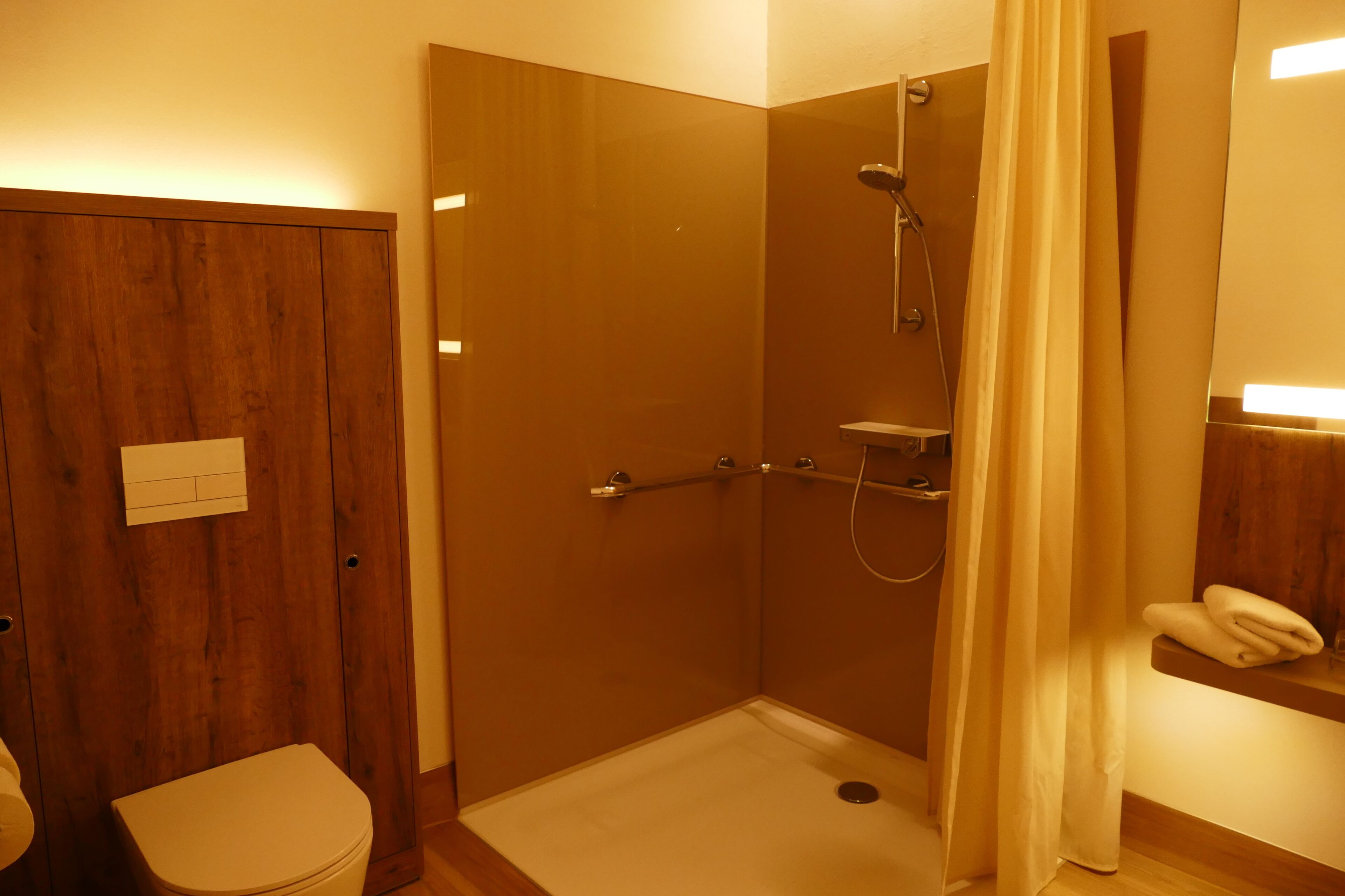 Un baño pequeño y funcional con puerta de madera, inodoro, ducha con mampara de vidrio y toallero.
