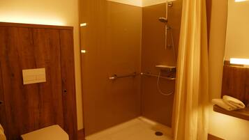 Un baño pequeño y funcional con puerta de madera, inodoro, ducha con mampara de vidrio y toallero.