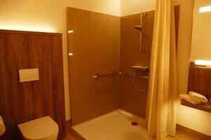 Un baño pequeño y funcional con puerta de madera, inodoro, ducha con mampara de vidrio y toallero.