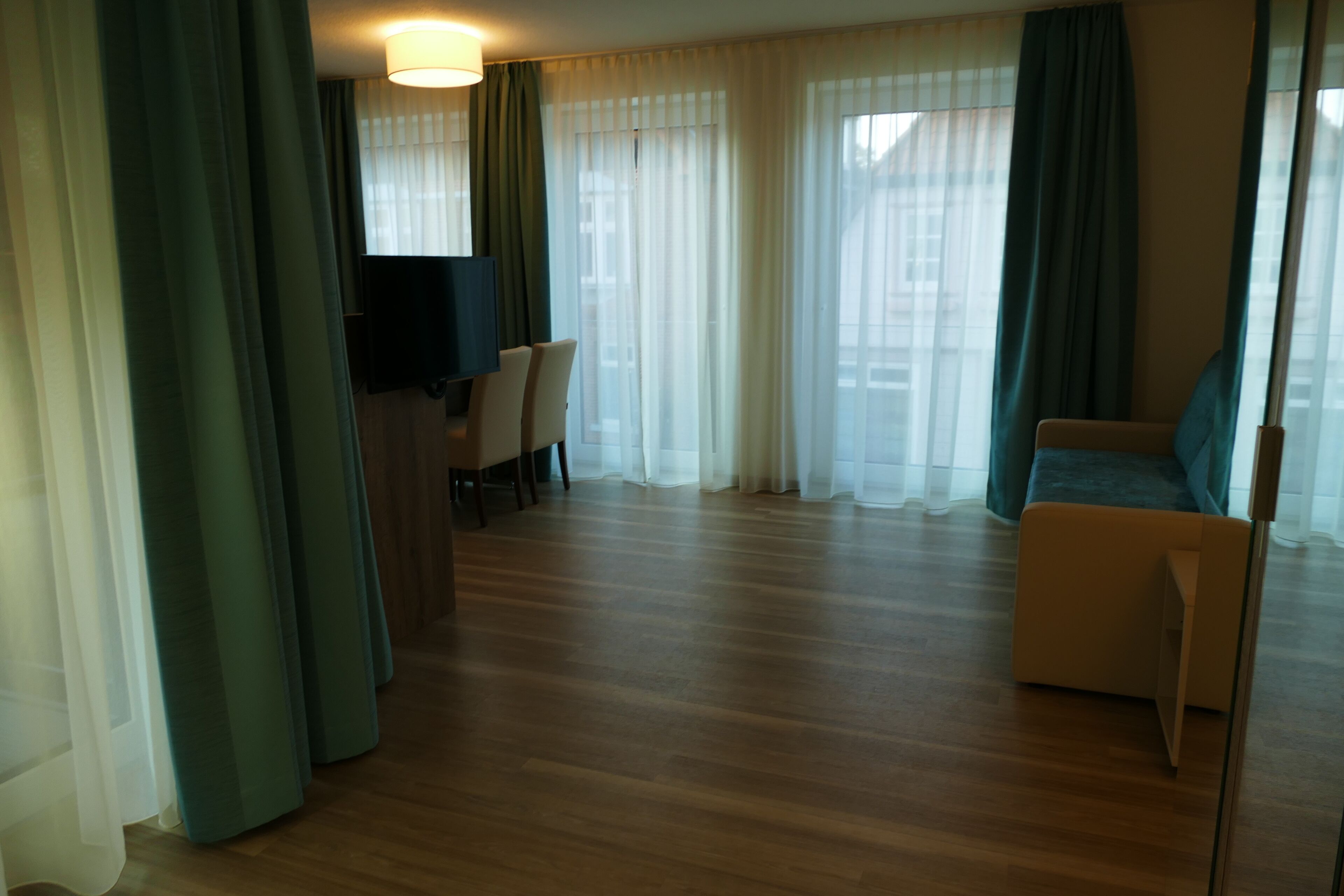 A hotel room with a wooden floor, a sofa, a TV, and a desk with chairs.