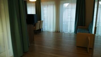 A hotel room with a wooden floor, a sofa, a TV, and a desk with chairs.