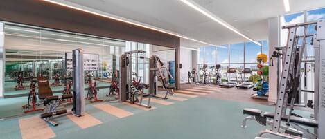 A modern gym with various exercise machines, large windows, and a clean, spacious layout.