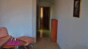 Une pièce avec un canapé rose, une petite table surmontée d’un tapis rose et une grande armoire en bois.