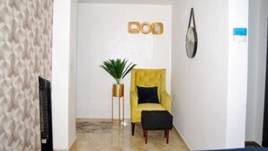 Een modern interieur met een gele fauteuil, een potplant en een decoratief object aan de muur.