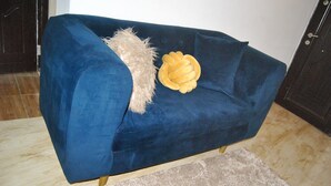 Een blauwe bank met een zachte deken en een decoratief kussen in een kamer met een betegelde vloer en een houten deur.