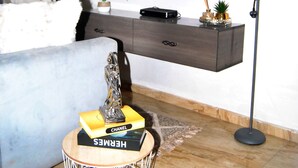 Una camera da letto con un letto, una TV fissata al muro, una lampada da terra, un comodino con dei libri e una pianta in vaso.
