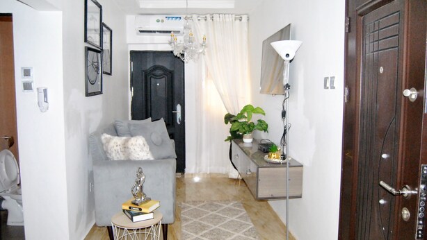 Un soggiorno moderno con un divano grigio, un tavolino, un lampadario, una pianta in vaso e una porta in legno.