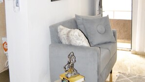 Un soggiorno moderno con un divano grigio, un piccolo tavolino con un libro e un oggetto decorativo, e un quadro raffigurante biciclette appeso al muro.