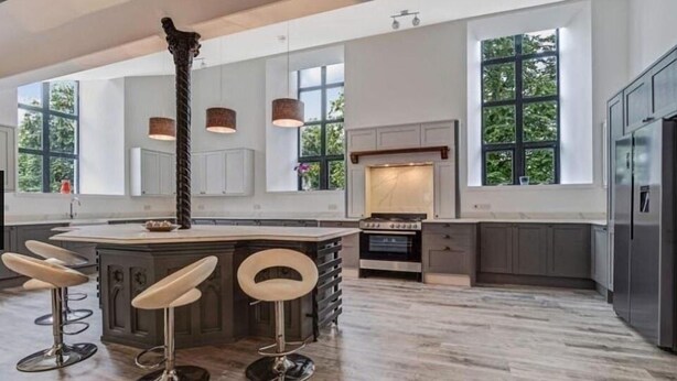 A modern kitchen with a central island, bar stools, a stove, and large windows. - East Church House (Strathaven)
