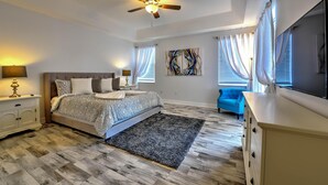 A bedroom with a bed, nightstands, a ceiling fan, a blue chair, and a TV. - Famosa Villa (Kissimmee)