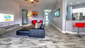 A modern living room with a sectional sofa, a ceiling fan, and a kitchen area with bar stools. - Famosa Villa (Kissimmee)