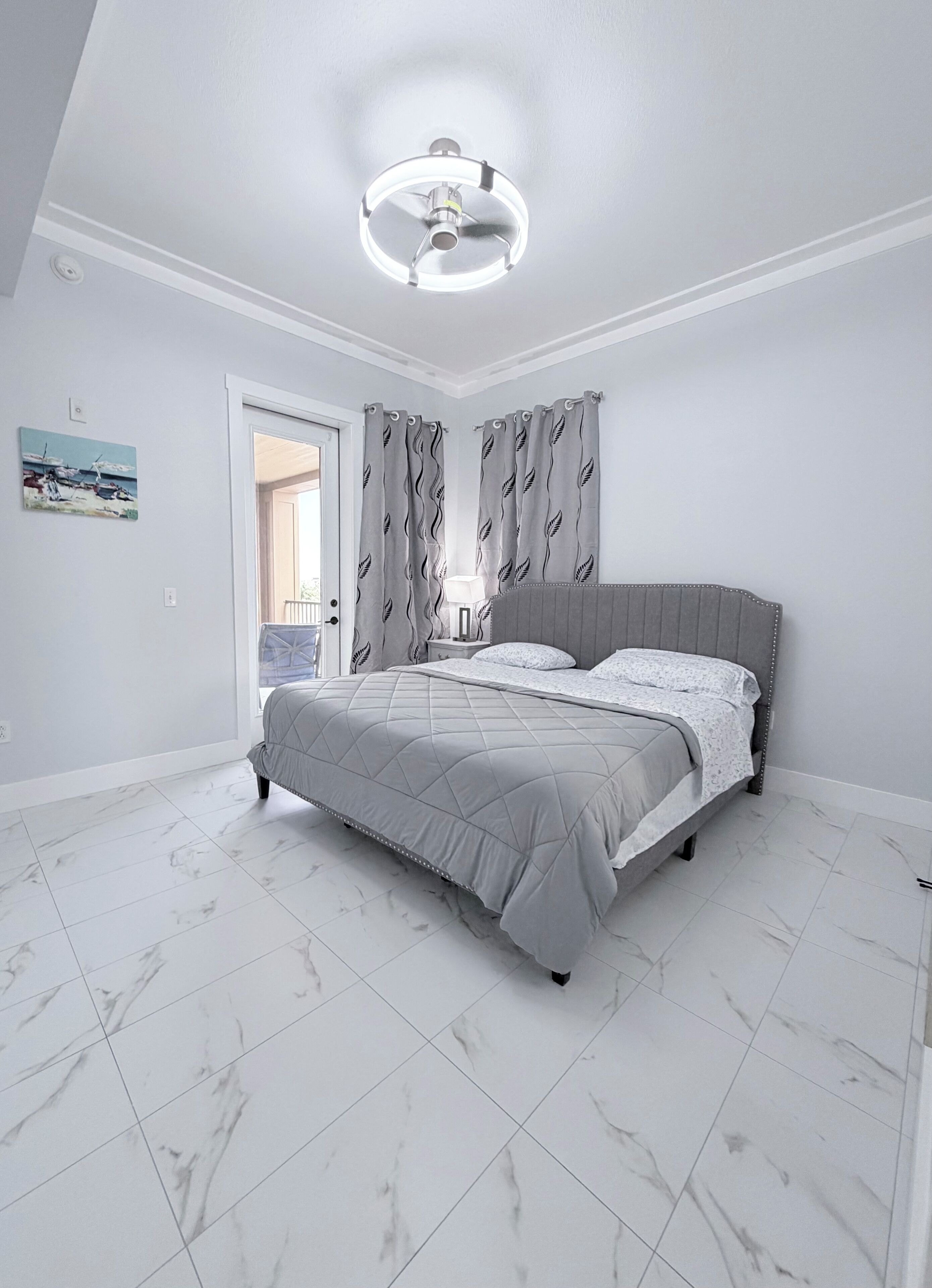 A bedroom with a bed, a ceiling fan, a door, and a painting on the wall.