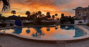 Piscina con vistas al atardecer, rodeada de palmeras y un edificio.