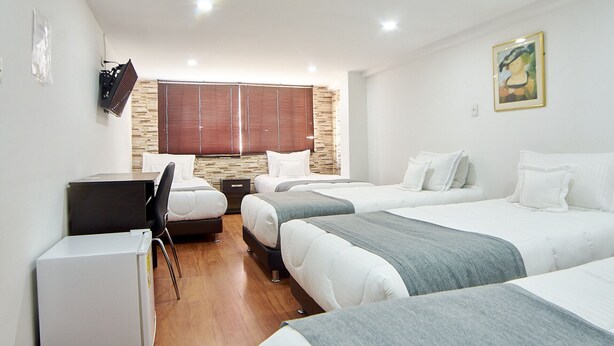 A hotel room with three beds, a desk, and a refrigerator.