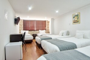 A hotel room with three beds, a desk, and a refrigerator. - Hotel Colonial Internacional (Bogotá)