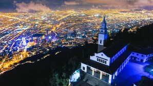 A night view of a cityscape with a prominent church tower and a building with a balcony.