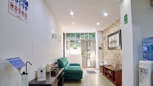 A reception area with a desk, a green sofa, a water dispenser, and a door leading to a balcony.