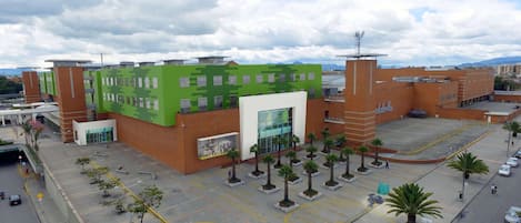 Um edifício moderno com fachada verde, um pátio central com palmeiras e uma área de estacionamento.