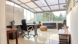 A modern office space with a glass ceiling, a desk with a computer, a black office chair, a sofa, and a bookshelf.